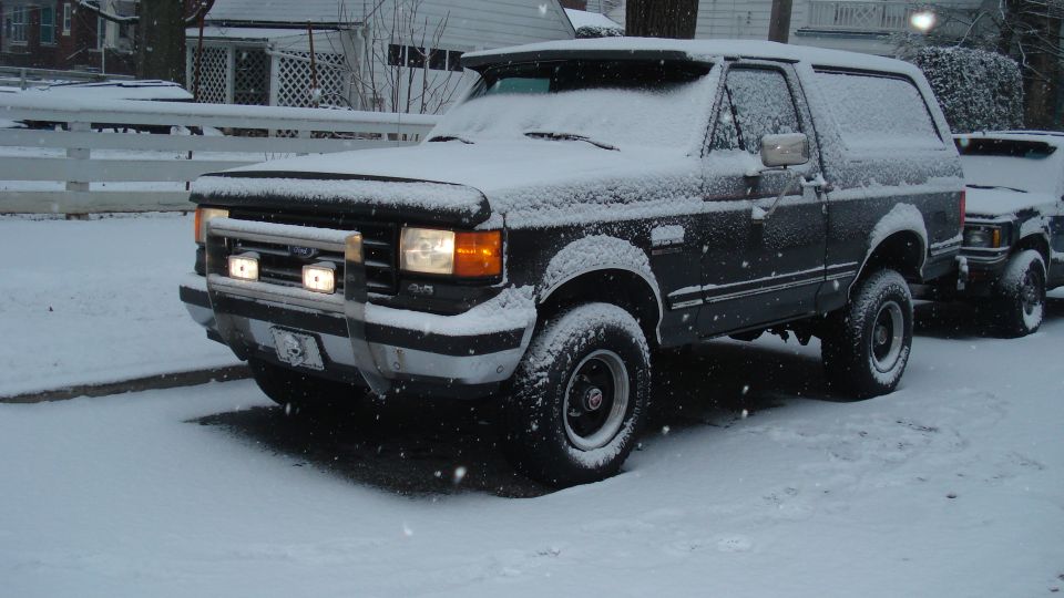 Dark Ford Bronco covered in snow, parked next to another vehicle