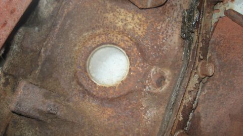 1988 Ford Bronco - This image shows a close-up view of a heavily rusted engine block casting, a circular plug and surrounding metal components.
