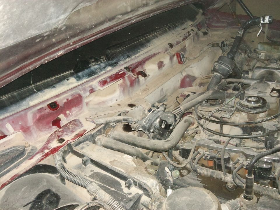 View of the wiper tray area and engine bay, showing hoses and wiring. The area is dusty and appears to be under the windshield