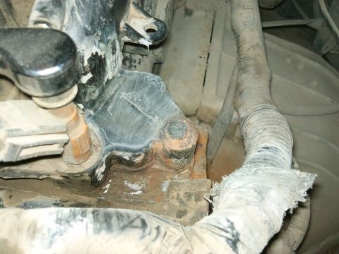 1998 Ford Crown Victoria - Close-up of a rusty bracket and mount bolt in a dusty engine bay, with chipped black paint, surface rust and a chrome-capped fitting at upp…