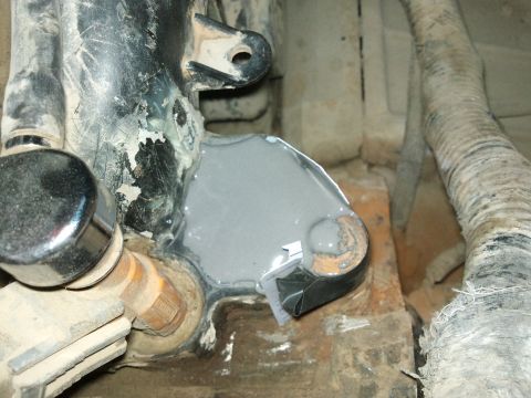 1998 Ford Crown Victoria - Underhood close-up of a chipped black-painted bracket and chrome-capped fitting with a pool of thick gray liquid, likely sealant or primer,…