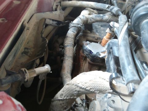 1998 Ford Crown Victoria - Tight shot down into the front corner of a maroon car's engine bay, showing dust-caked heater and A/C hoses, a fabric-sleeved braided line,…