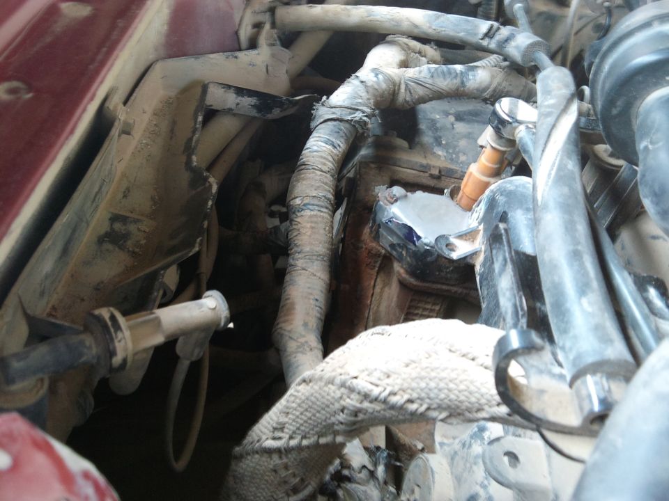 Dusty hoses, braided line and rusty core support in a maroon car's engine bay corner