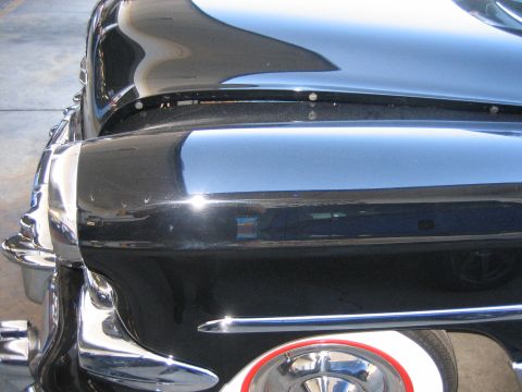 1998 Ford Crown Victoria - Detail of a deep-black classic car's front fender curve, chrome trim, and a wide-whitewall tire with a red wheel.