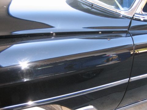 1998 Ford Crown Victoria - Reflective black bodywork of a classic car showing the door, fender, and a horizontal chrome side spear.