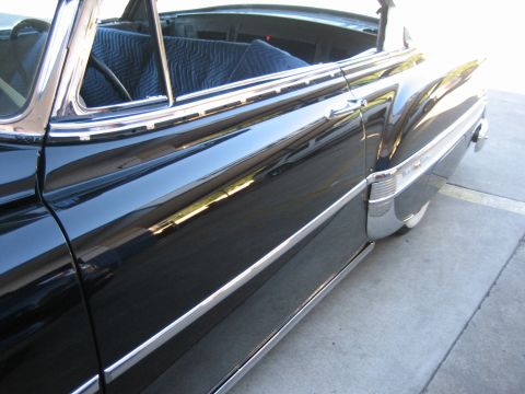 1998 Ford Crown Victoria - Profile detail of a glossy black classic car's lower body, rocker chrome, and a chrome-trimmed taillight.