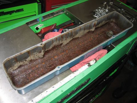 1998 Ford Crown Victoria - long aluminum oil pan or valley cover heavily coated in rusty sludge rests across a green rolling tool chest.