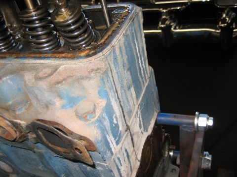 1998 Ford Crown Victoria - corner of a worn blue-painted inline engine head with valve springs, surface rust, and a support arm at right.