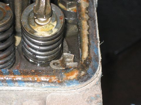 1998 Ford Crown Victoria - Close-up of a rust-streaked blue engine head corner showing a valve spring, mounting tab, and gasket edge.