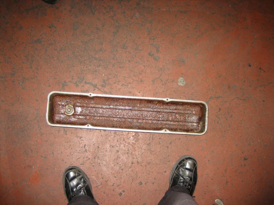 Rust-filled long engine valley cover on a concrete floor between boots
