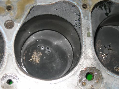 1998 Ford Crown Victoria - Top-down view of two cylinder bores with a worn piston and green-marked valve seats on an engine block deck.