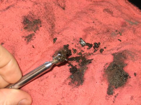 1998 Ford Crown Victoria - hand uses a slender metal pick to scrape black carbon deposits and sludge onto a red shop towel.