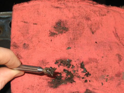 1998 Ford Crown Victoria - hand holds a thin metal pick above a red shop towel marked with black grease and carbon smears.