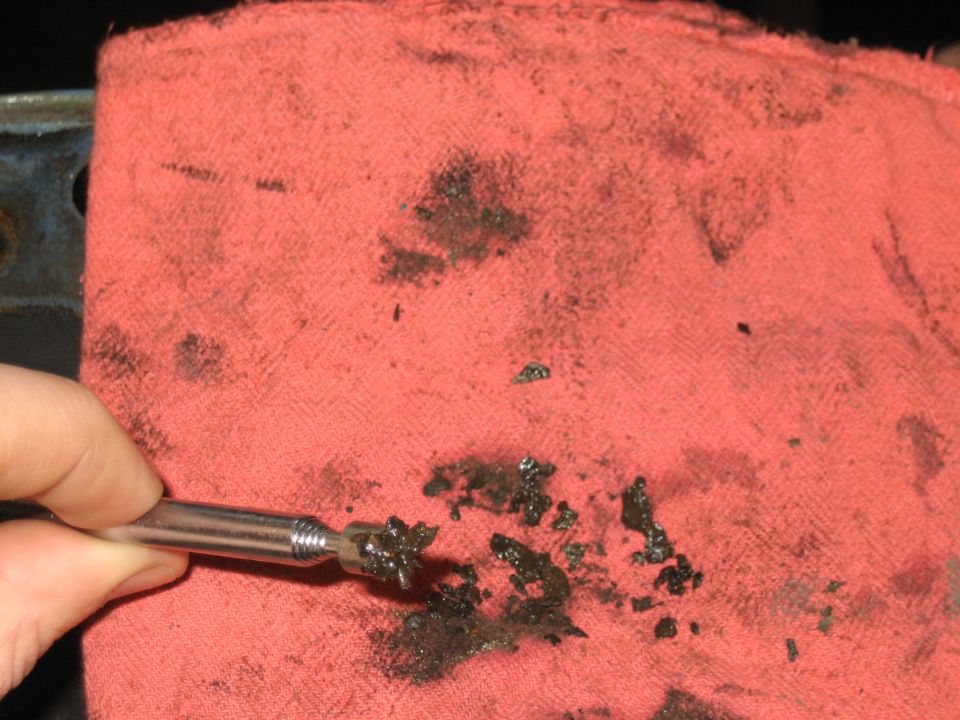 Hand holding metal pick over a red shop rag with black grease smears