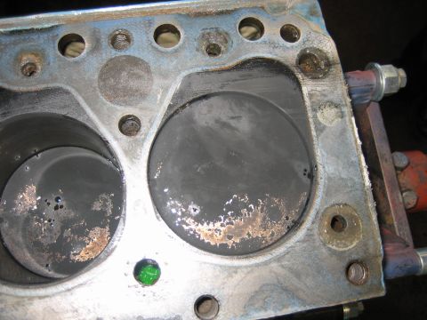 1998 Ford Crown Victoria - Close view of an engine block deck with two cylinder bores showing surface scoring, corrosion and a green core plug.