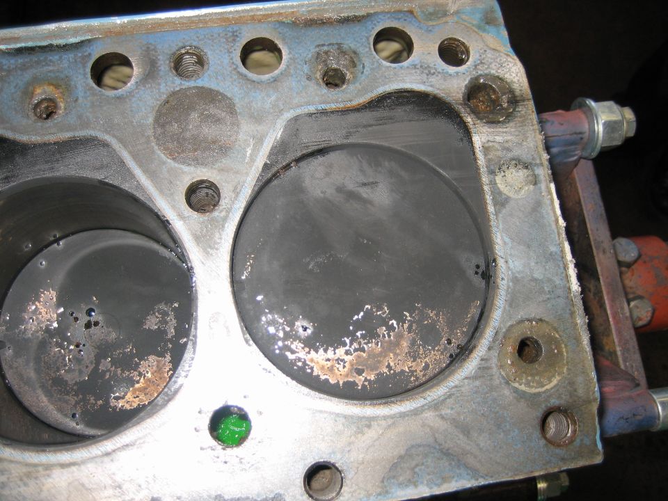 Engine block deck with two cylinder bores showing scoring and green plug