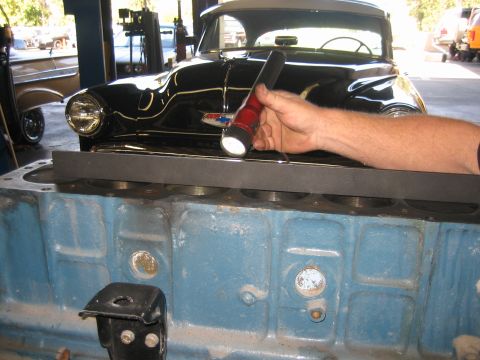 1998 Ford Crown Victoria - hand holds a flashlight over a blue painted engine block in a shop, with a black classic car parked behind.