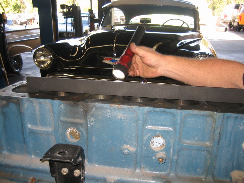 Hand with flashlight over blue engine block in shop with black car behind