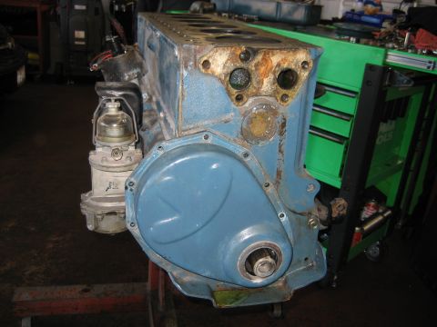 1998 Ford Crown Victoria - blue painted engine block mounted on a stand with timing cover and fuel pump, next to a green tool chest in a shop.