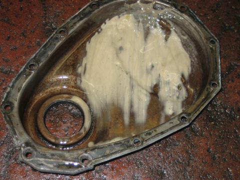 1998 Ford Crown Victoria - engine timing cover with seal bore, coated in white assembly grease, sitting on a red brick shop floor.
