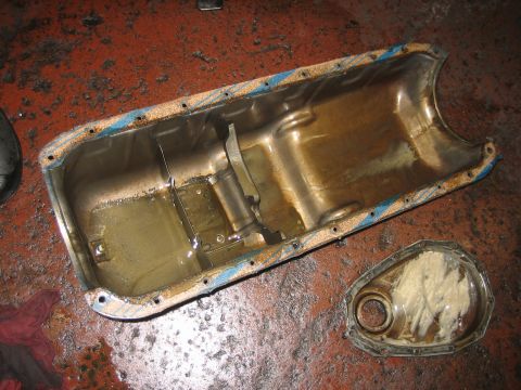 1998 Ford Crown Victoria - long engine oil pan and a grease-coated timing cover laid out on a red brick shop floor.