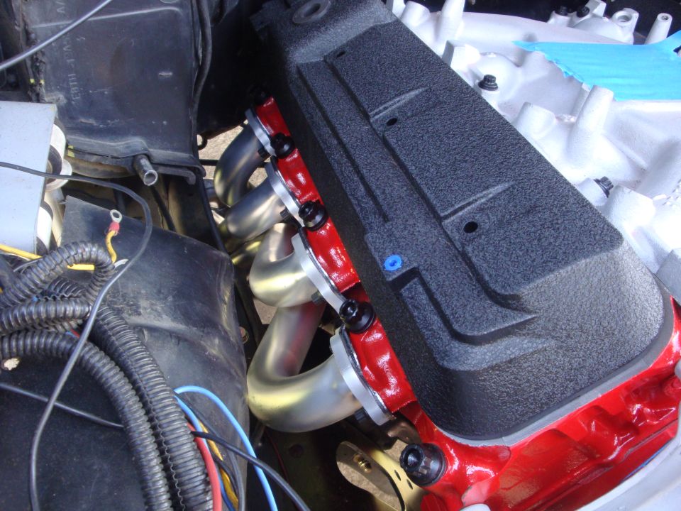 Close-up of a car engine's black valve cover and red gasket with silver exhaust headers