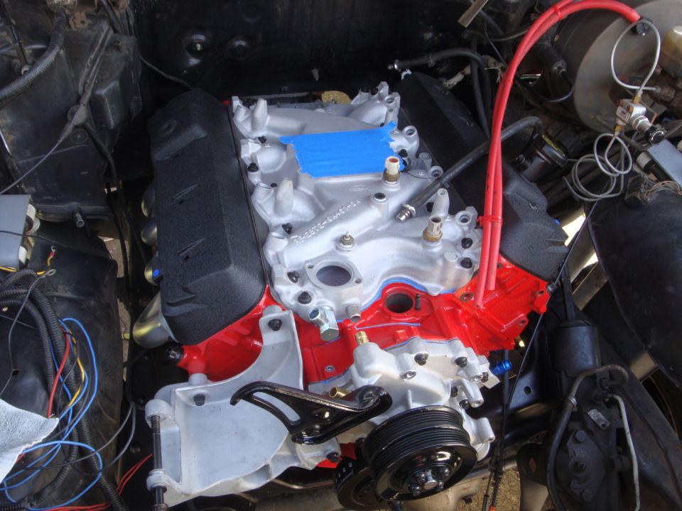 Engine bay with a freshly painted red and silver engine, red spark plug wires, and blue tape on the intake manifold