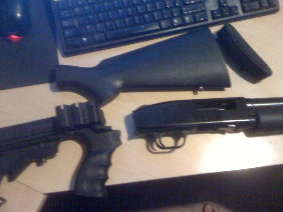 Disassembled black shotgun with pistol grip and stock on a wooden surface next to a keyboard