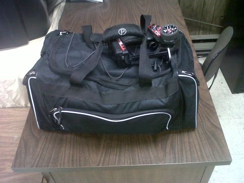 2011 Ford 427 - A black duffel bag sits on a wooden desk with various items placed on top of it.
