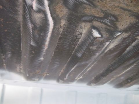 1979 Ford Bronco - The underside of a vehicle, showing ribbed metal construction and signs of wear and tear.