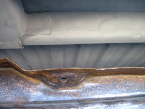 1979 Ford Bronco - The underside of a vehicle reveals a rusted frame and painted structural elements.