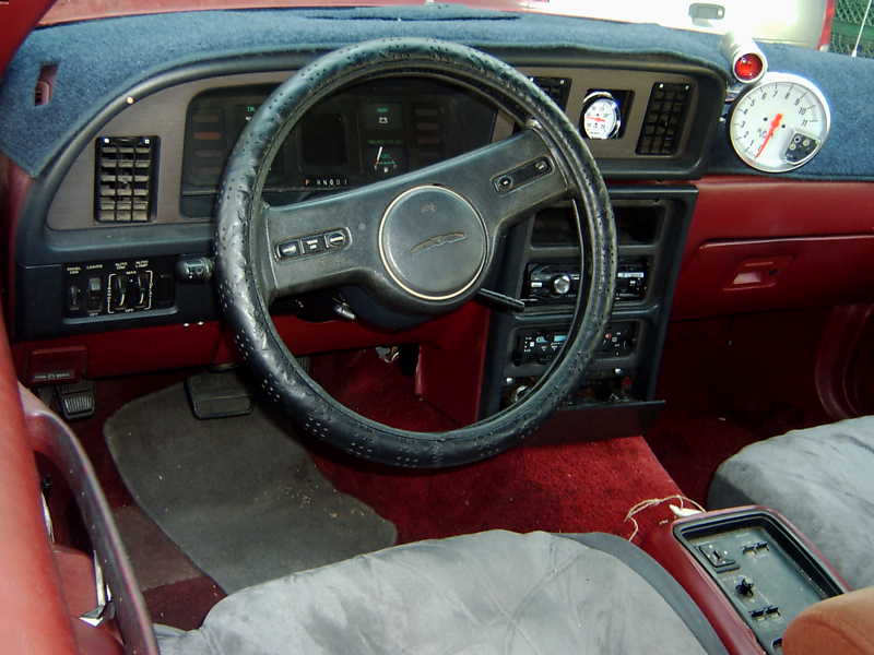 1987 Ford Thunderbird interior with red upholstery, black steering wheel, and aftermarket gauges