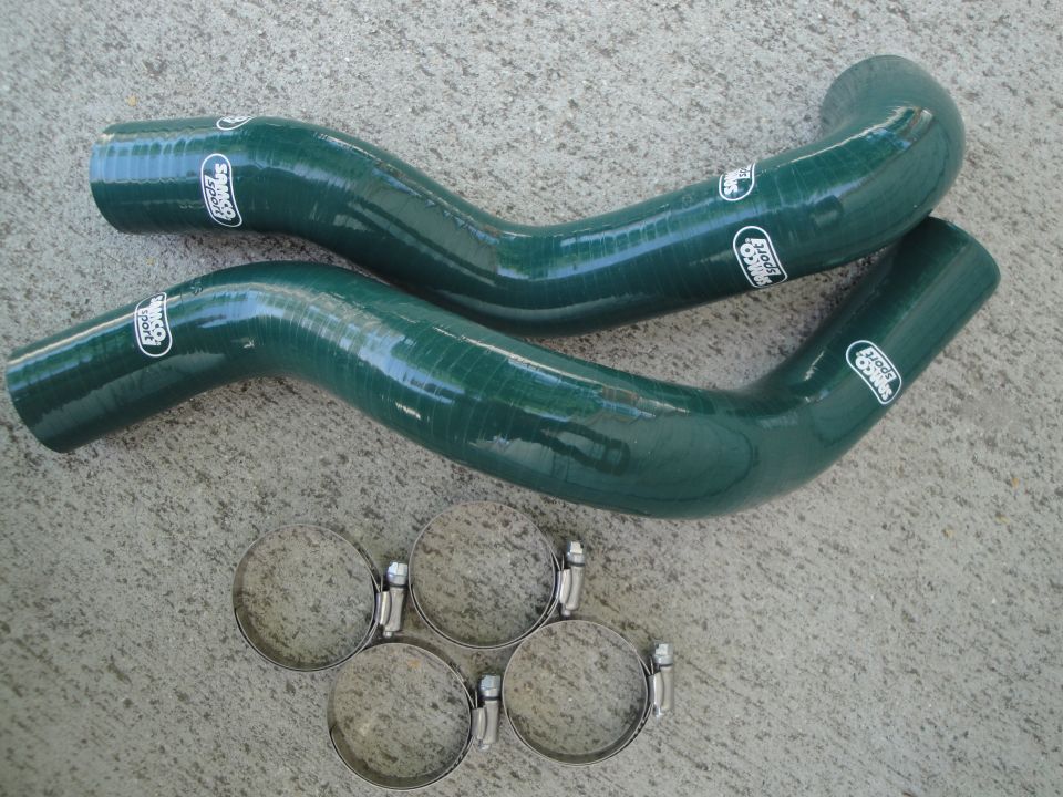 Two green silicone hoses with white "Samco Sport" logos and four hose clamps on a concrete surface