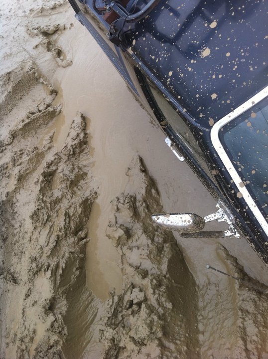 Black SUV with mud splatters stuck in deep mud, showing tire tracks and a side mirror