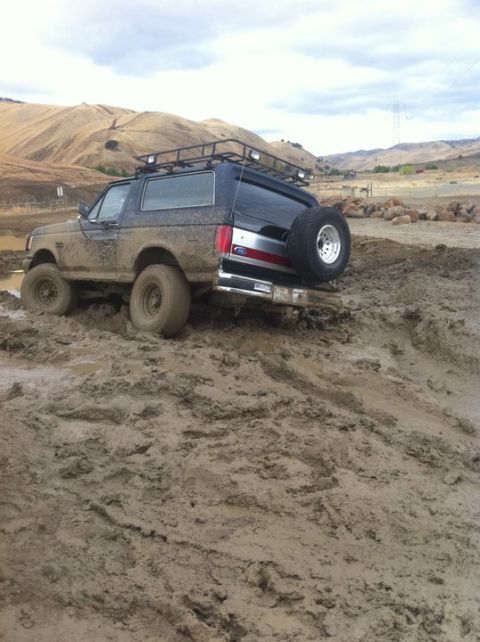 1990 Ford Bronco - A muddy 1990 Ford Bronco navigates a challenging off-road terrain.