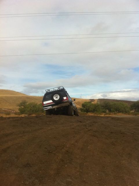 1990 Ford Bronco - This 1990 Ford Bronco is seen tilted on a muddy incline, its rear profile with a spare tire and roof rack.