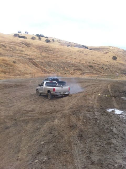1990 Ford Bronco - A silver pickup truck transports a black car across a muddy, off-road terrain.