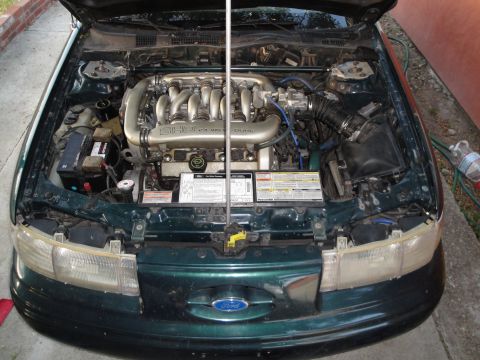 1995 Ford Taurus - The engine bay of a 1995 Ford Taurus, its V6 DOHC engine and various hoses.