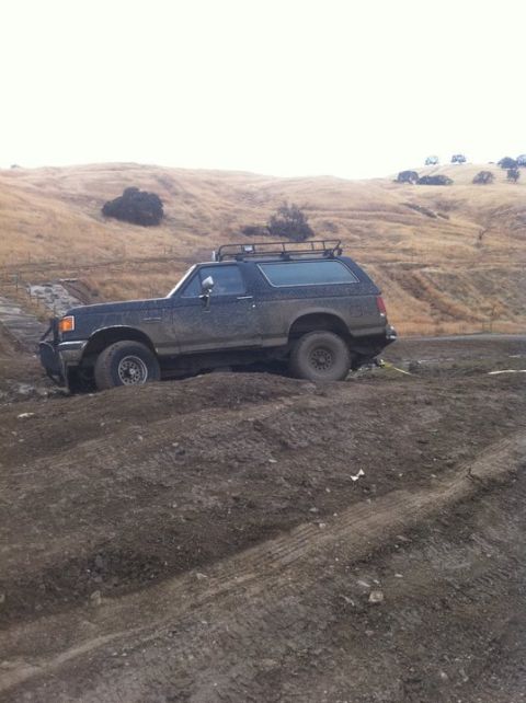 1990 Ford Bronco - A muddy Ford Bronco is stuck in the dirt on a hillside.