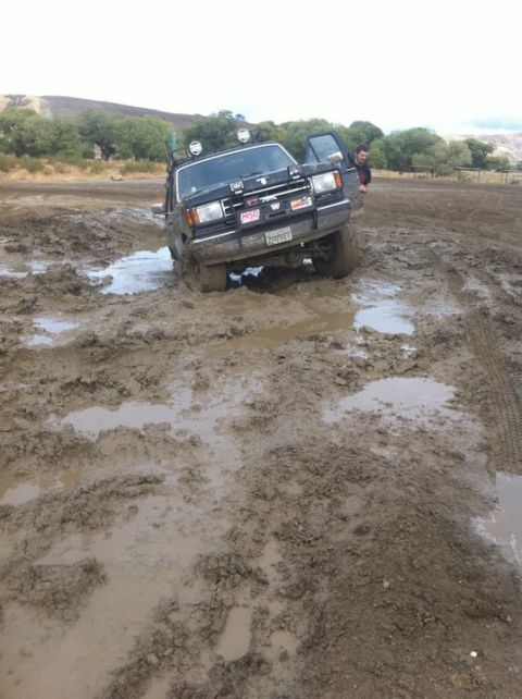 1990 Ford Bronco - A 1990 Ford Bronco navigates a muddy off-road course, with its front tires deep in the mire.