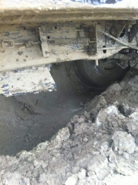 1990 Ford Bronco - A vehicle's undercarriage is deeply mired in thick mud, with the tire barely visible.