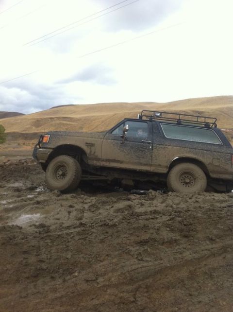 1990 Ford Bronco - This Ford Bronco is deep in the mud, with its tires struggling for traction on the slick terrain.