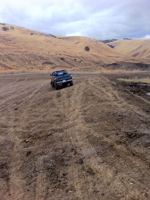1990 Ford Bronco - A pickup truck navigates a challenging dirt path through a dry, hilly landscape under a cloudy sky.