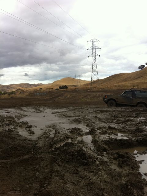 1990 Ford Bronco - A 1990 Ford Bronco navigates a muddy terrain under a cloudy sky.