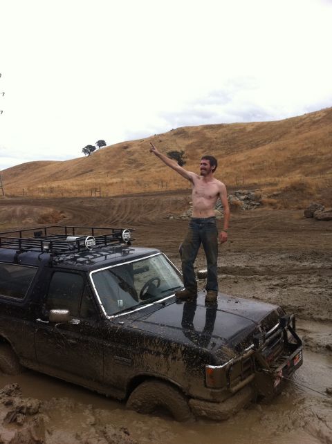 1990 Ford Bronco - Man stands on a 1990 Ford Bronco that is stuck in the mud. The vehicle is covered in mud.