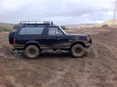 1990 Ford Bronco - Muddy 1990 Ford Bronco with roof rack and spare tire on the back is seen off-roading.