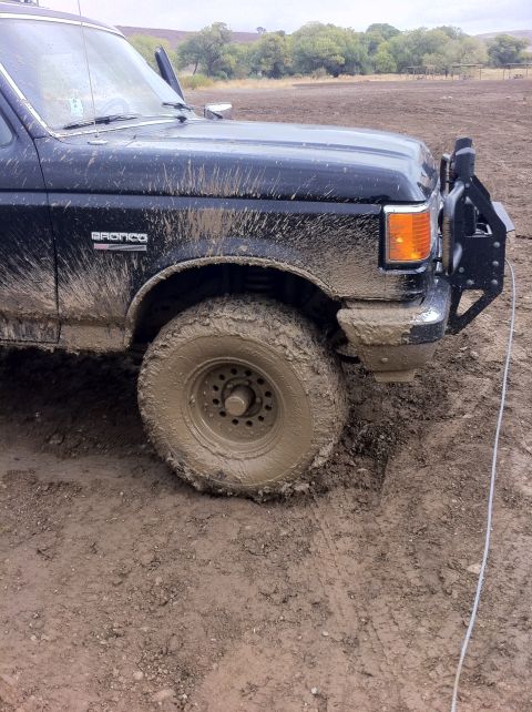 1990 Ford Bronco - Mud-covered Ford Bronco with its front wheel stuck in the mire, showing an aftermarket bumper and spare tire mount.