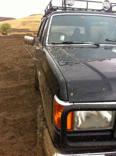 1990 Ford Bronco - This black SUV, equipped with a roof rack and auxiliary lights, navigates a muddy off-road terrain.