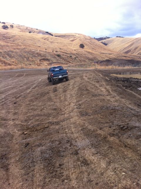 1990 Ford Bronco - A pickup truck navigates a muddy, off-road terrain under a cloudy sky.