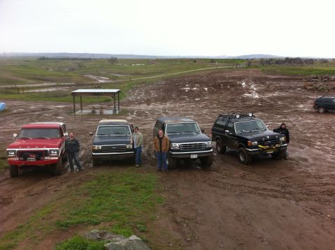 1990 Ford Bronco - Several off-road vehicles are gathered in a muddy, outdoor area.